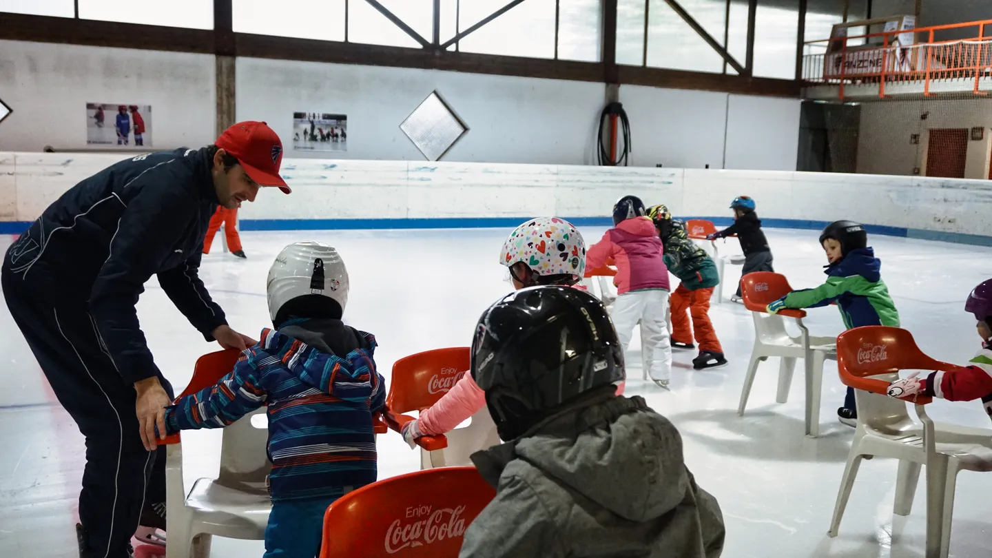 Kinder mit Helmen und ein Trainer bei einer gemeinsamen Übung auf dem Eis.