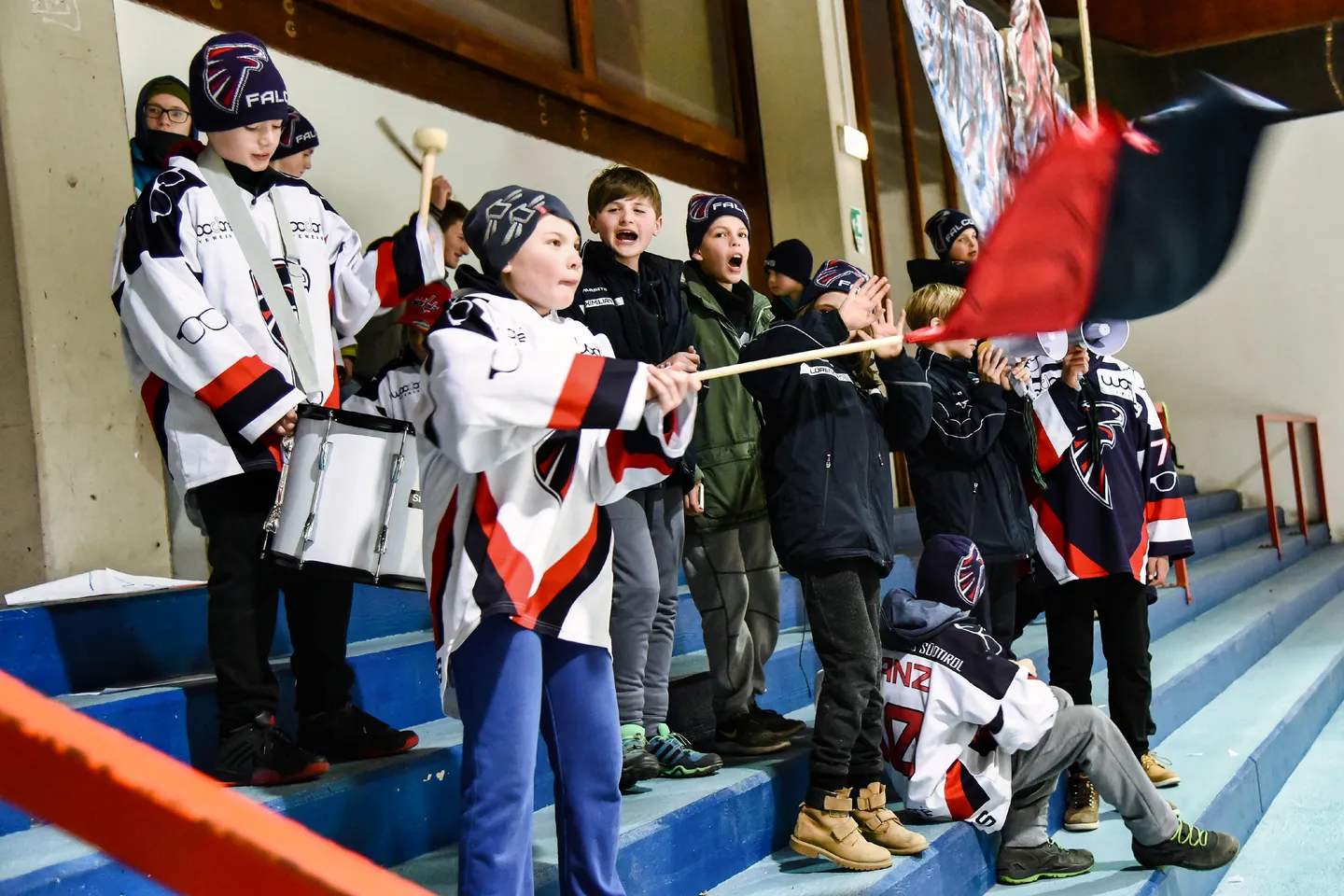 Junge Falcons-Fans und Spieler feuern gemeinsam mit einer Vereinsfahne an.
