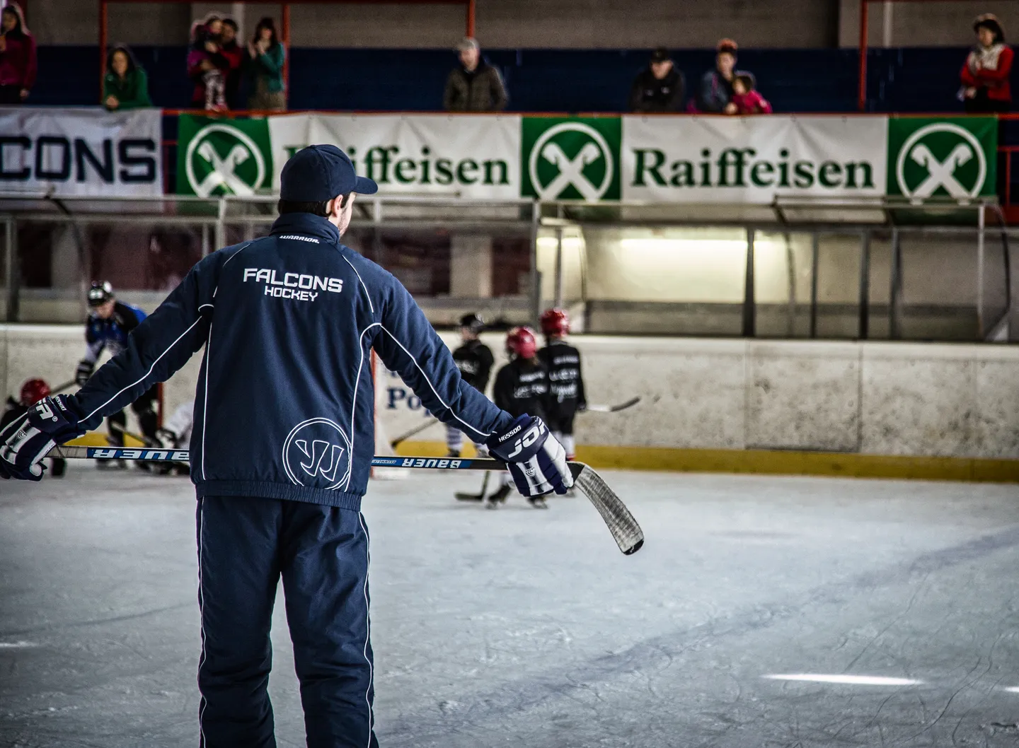 Ein Trainer mit Falcons-Jacke begleitet das Training auf dem Eis.